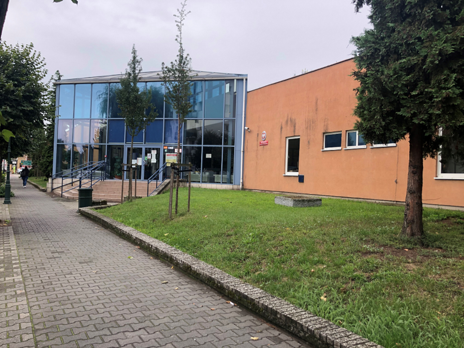 Na zdjęciu przeszklona część wejścia do budynku pozostała część budynku w elewacji koloru ceglastego