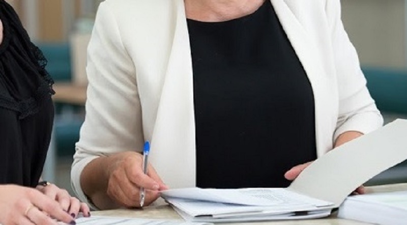 Na zdjęciu pani trzyma w ręku plik dokumentów