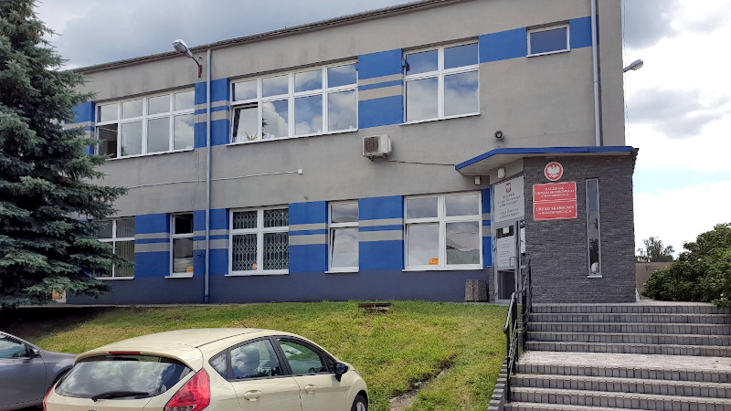 Budynek Urzędu Skarbowego w Białobrzegach, wejście, schody i dwa samochody.  