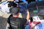 Funkcjonariusz w kamizelce z napisem Służba Celno-Skarbowa trzyma w ręce opakowanie w nieogrinalną koszulką