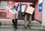 Dwóch pracowników w strojach Świętego Mikołaja na schodach Urzędu Skarbowego w Olkuszu niesie prezenty.