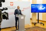 Wiceminister Artur Soboń stoi za mównicą, w tle logo MF