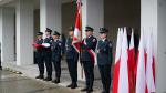 Uroczysty apel z udziałem funkcjonariuszy w mundurach oraz polskimi flagami, jedna osoba niesie flagę państwową.