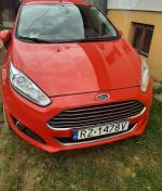 Samochód osobowy Ford Fiesta w kolorze czerwonym. Przód pojazdu z widoczną tablicą rejestracyjną