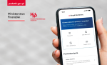 Na szarym tle dłoń trzymająca smartfon na jego ekranie aplikacja e-Urząd Skarbowy