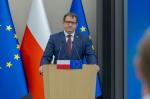 Grafika dekoracyjna, mężczyzna przy mównicy, w tle ekran multimedialny z wyświetloną prezentacją 