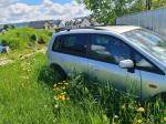 Samochód osobowy Mazda Premacy, kombi w kolorze srebrnym, rok produkcji 2004, wgniecenia w karoserii na nadkolu, tapicerka foteli materiałowa, wyeksploatowane wnętrze z widocznymi przetarciami na kierownicy i fotelu kierowcy.