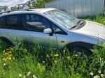 Samochód osobowy Mazda Premacy, kombi w kolorze srebrnym, rok produkcji 2004, wgniecenia w karoserii na nadkolu, tapicerka foteli materiałowa, wyeksploatowane wnętrze z widocznymi przetarciami na kierownicy i fotelu kierowcy.
