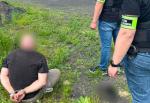 Mężczyzna z kajdankami na rękach siedzi na trawie, obok stoją dwaj funkcjonariusze Służby Celno-Skarbowej