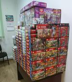 Zdjęcie przedstawia pomieszczenie, w którym na biurku ułożono stos pudełek z klockami.